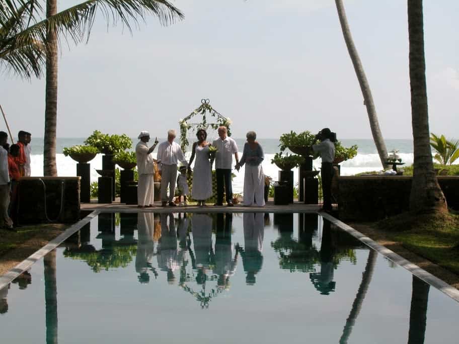 Wedding Ceremony at Apa Villa - the couple with witnesses stand in front of a swimming pool with the ocean and palm trees behind them