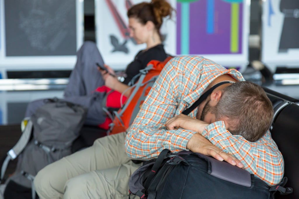 Passengers waiting for the air flight at airport terminal Man and woman sitting in chairs line sleeping browsing smart phone internet casual dress code heavy boots backpacks luggage building interior