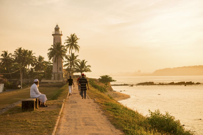 A few people walking at sunrise on the ramparts of Galle Fort next to the ocean