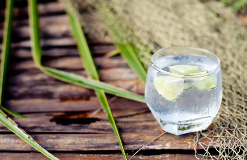 Gin tonic in glass with ice and lime slice and frangipany flower on a wooden background
