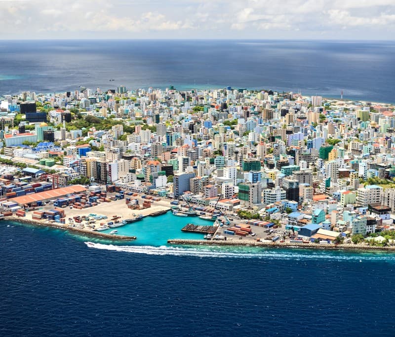 overhead view of male with densely pack buildings surrounded by blue ocean