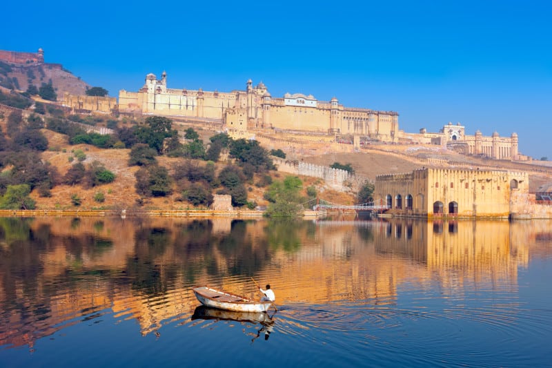 View of the Amber Fort with a lake and fisherman in the foreground and blue sky in the background