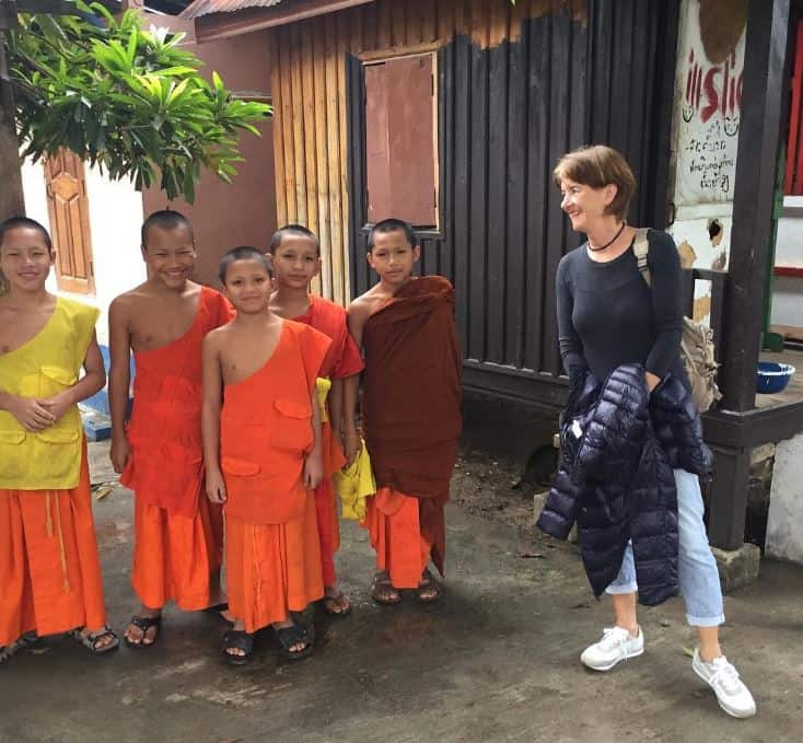 a smiling western tourist stands next to a group of young monks in Thailand