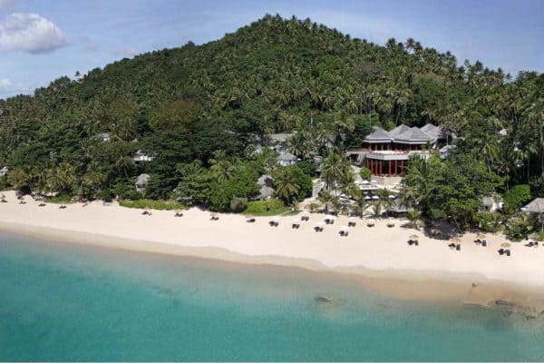 View from above of the beach of Surin Phuket. Clear blue sea, white sand beach and forest clad hill.