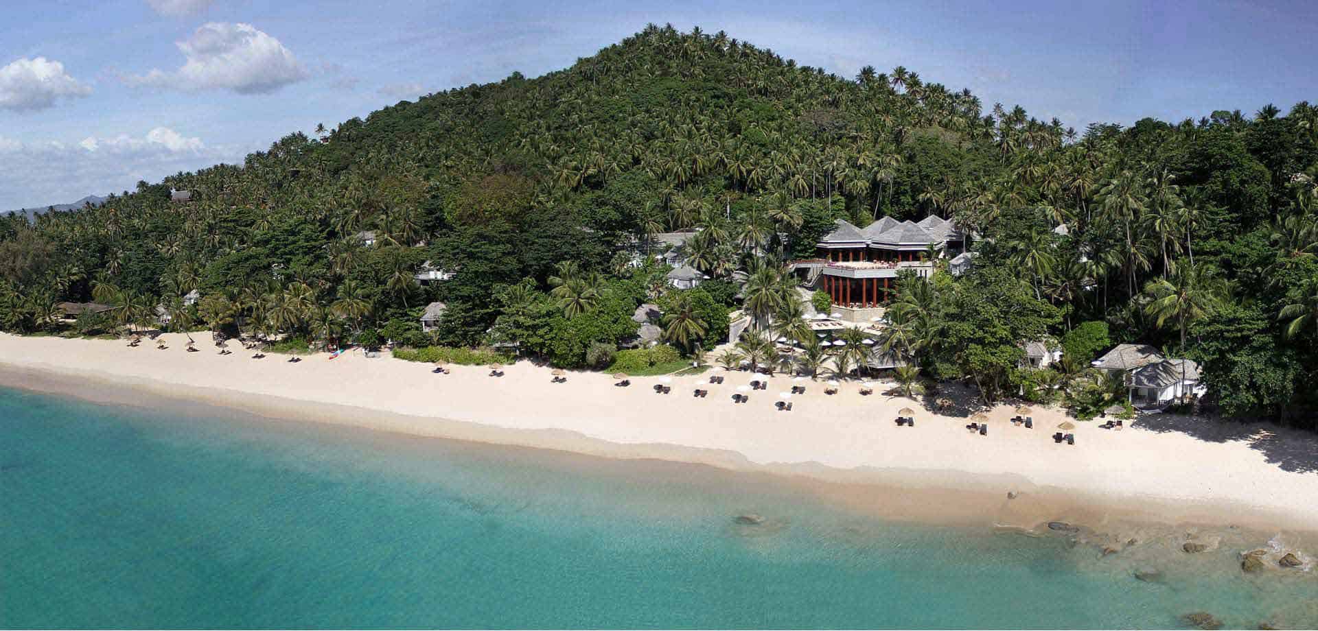 View from above of the beach of Surin Phuket. Clear blue sea, white sand beach and forest clad hill.