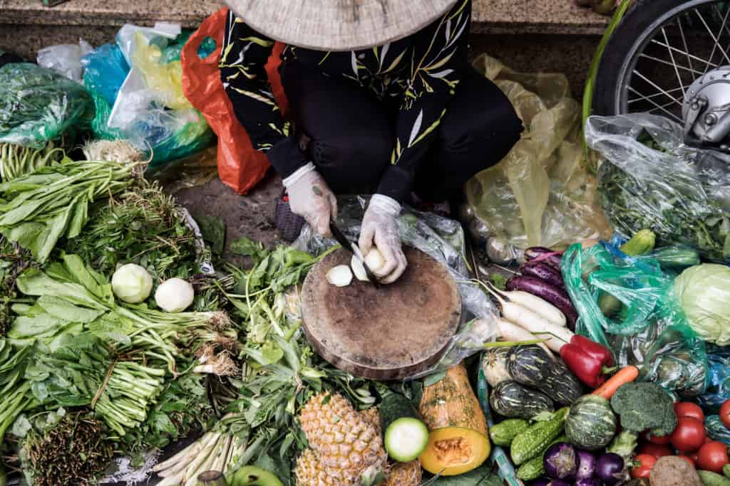 Hawker with conical hat in Hanoi cutting up fruit and vegetable