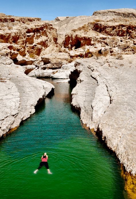 A person swimming in Wadi Bani Khalid - a narrow waterway of green water surrounded by a canyon