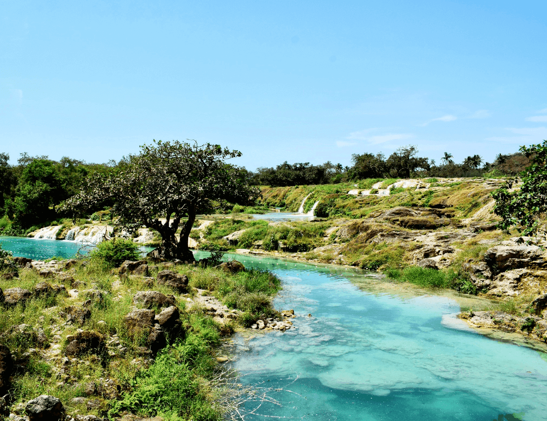 A Wadi in Jebel Samhan near Salalah - blue clear water surrounded by lush green scenery and blue sky