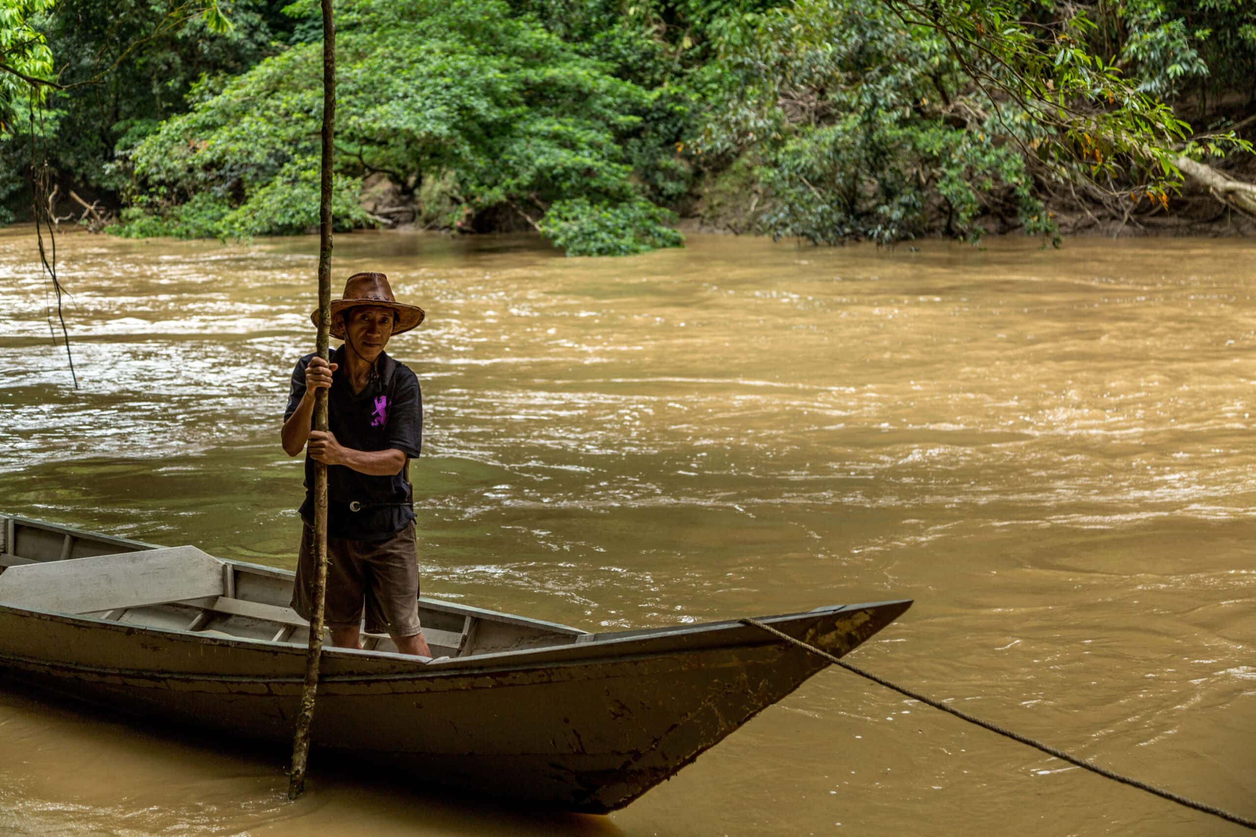 Man standing in wooden boat in the Kinabatangan River with jungle backdrop in Borneo