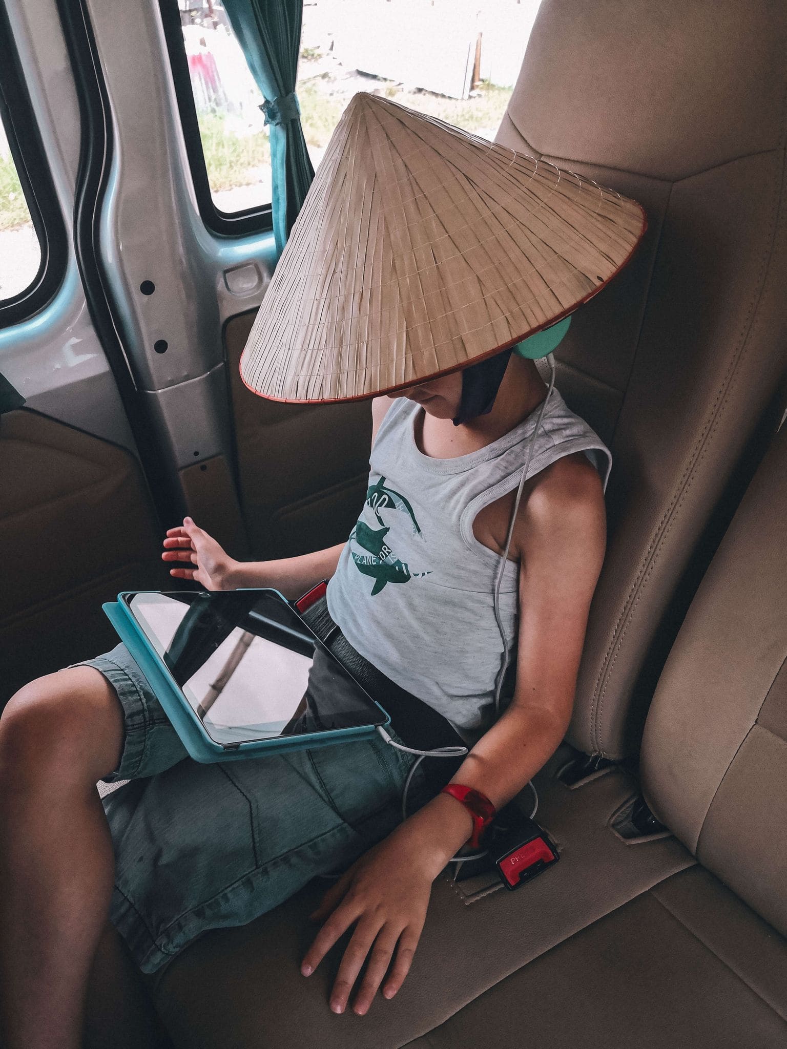 Child wearing traditional vietnamese conical hat whilst on his tablet