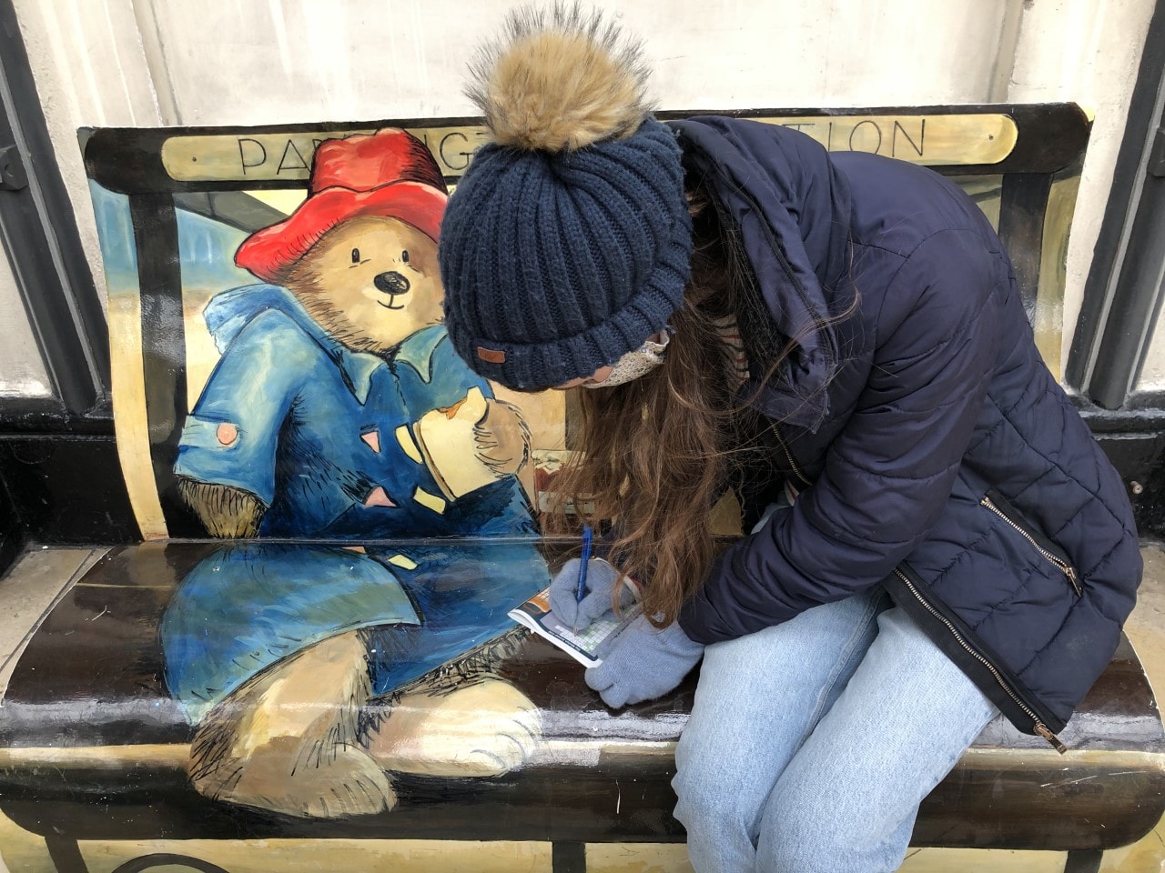 Woman completing a treasure trail map on a paddington bear bench in London