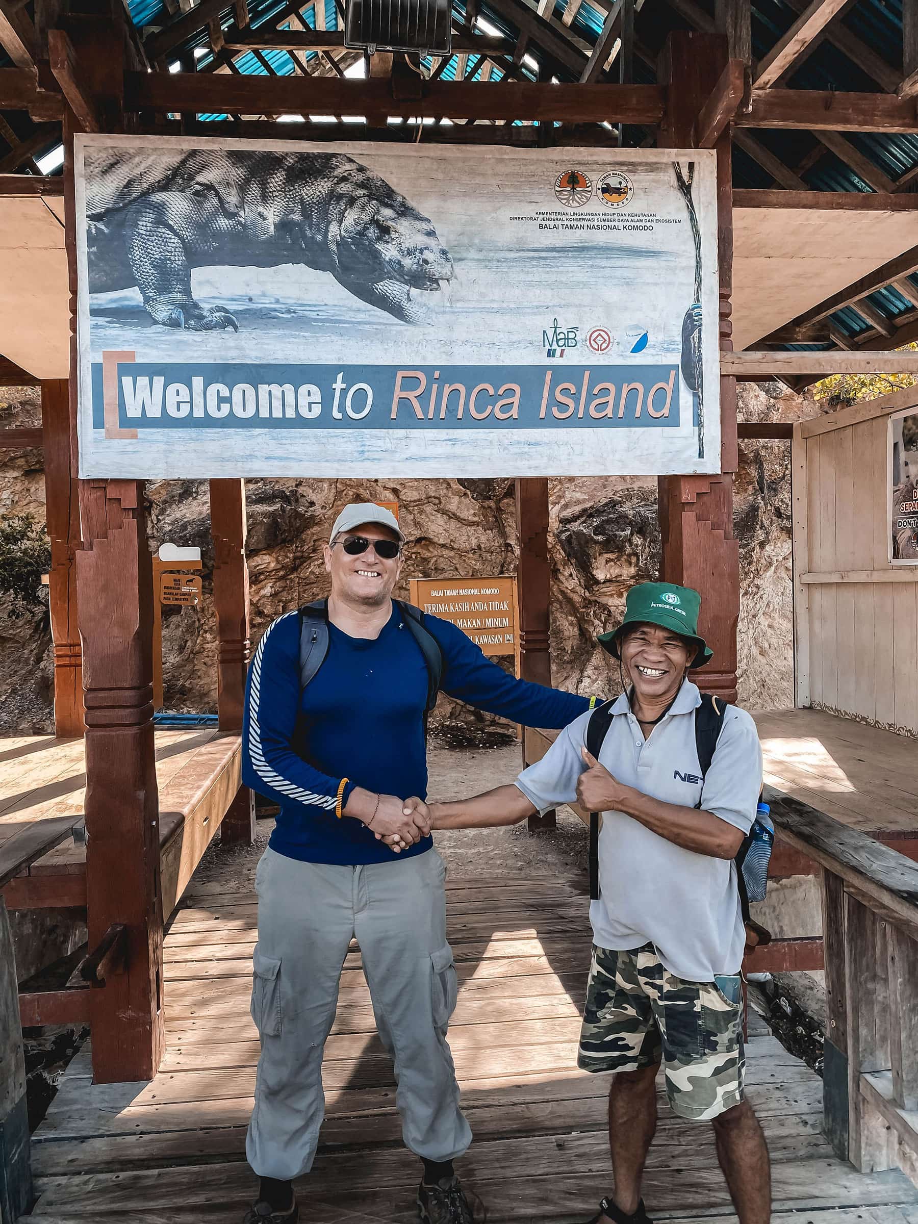 Traveller shaking hands with a guide on wooden walkway under a sign for rinca island