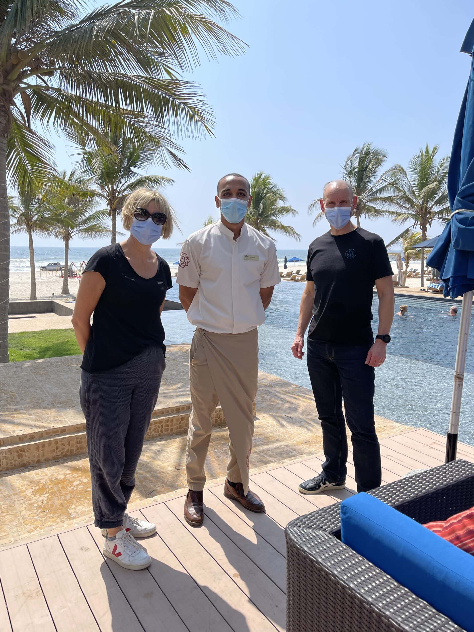 travellers and hotel general manager wearing masks with beach in the background