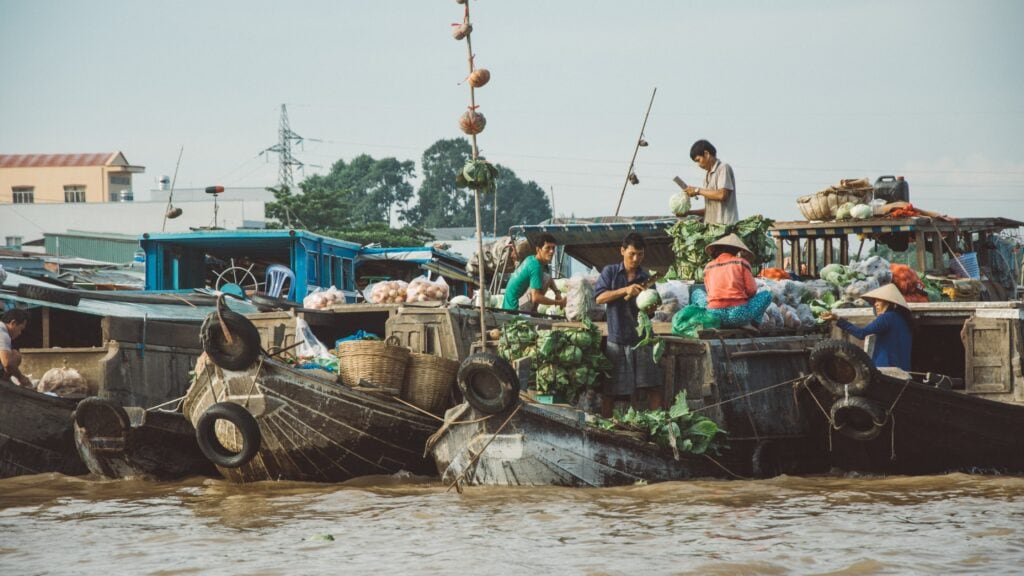 Men on boats displaying fresh produce on sale at Cai Rang floating market in Vietnam.