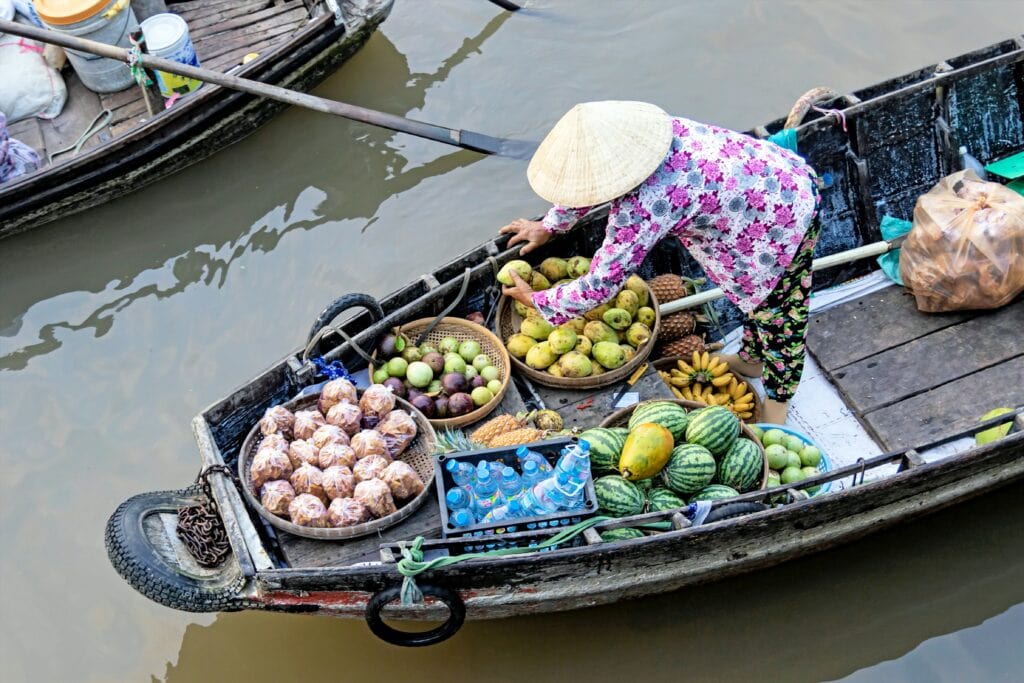 Woman standing on a boat with fresh fruit in large bowls at Can Tho floating market, Vietnam.