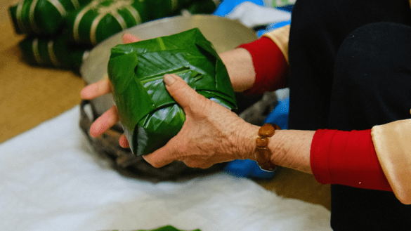 Woman wrapping a traditional Banh Chung in large banana leaves.