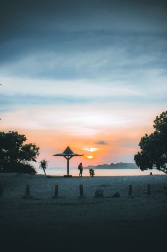 A person standing on Batu Bengkung Beach at sunset