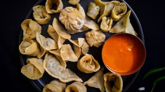 A plate of Momos (steamed buns) served with an orange chutney