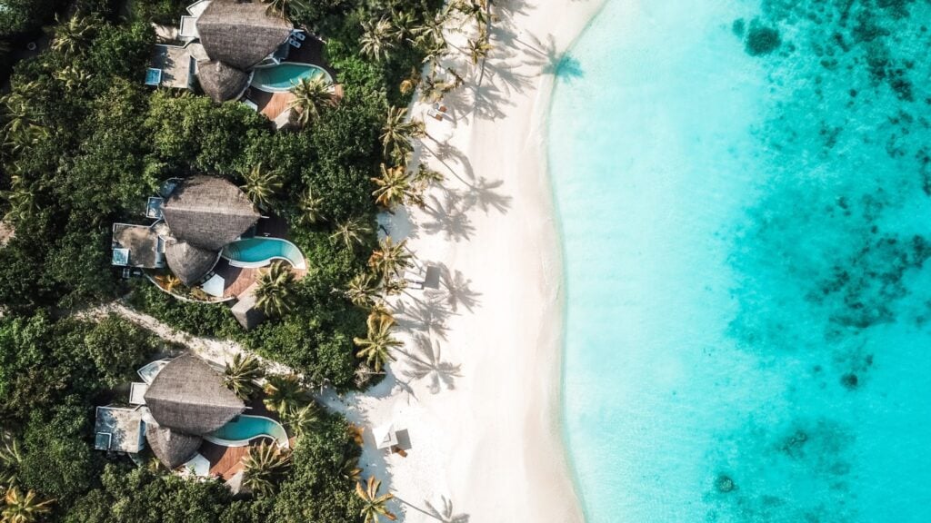 Aerial shot of Villas with private swimming pools leading to white sand and turquoise water