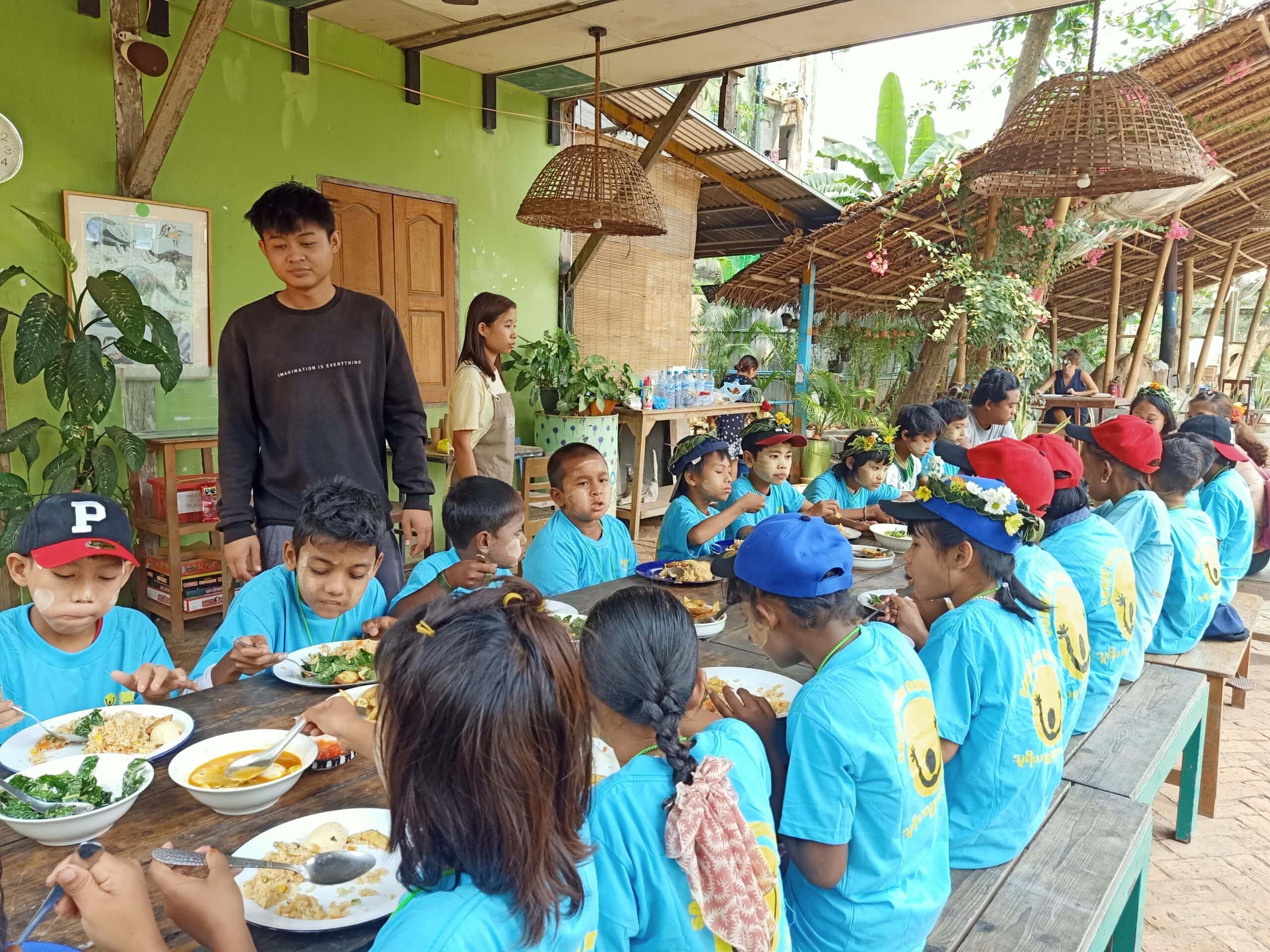 Happy children gather round a table eating an organic meal at Kokkoya Organic Farm, Yangon, Myanmar