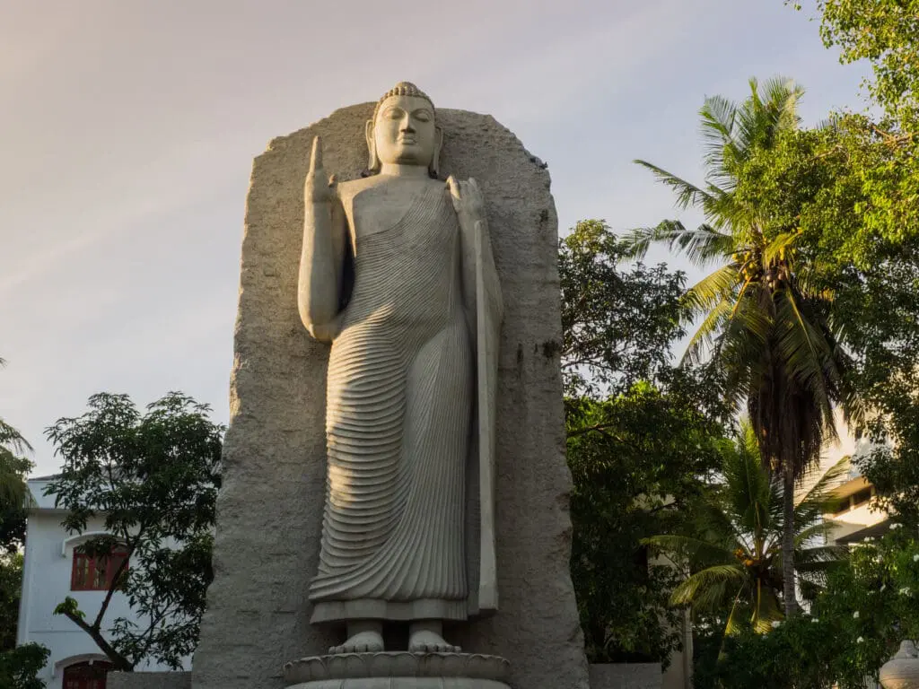 The standing Buddha statue at the Cinnamon Gardens are, Colombo, Sri Lanka, in the evening with trees in the background.