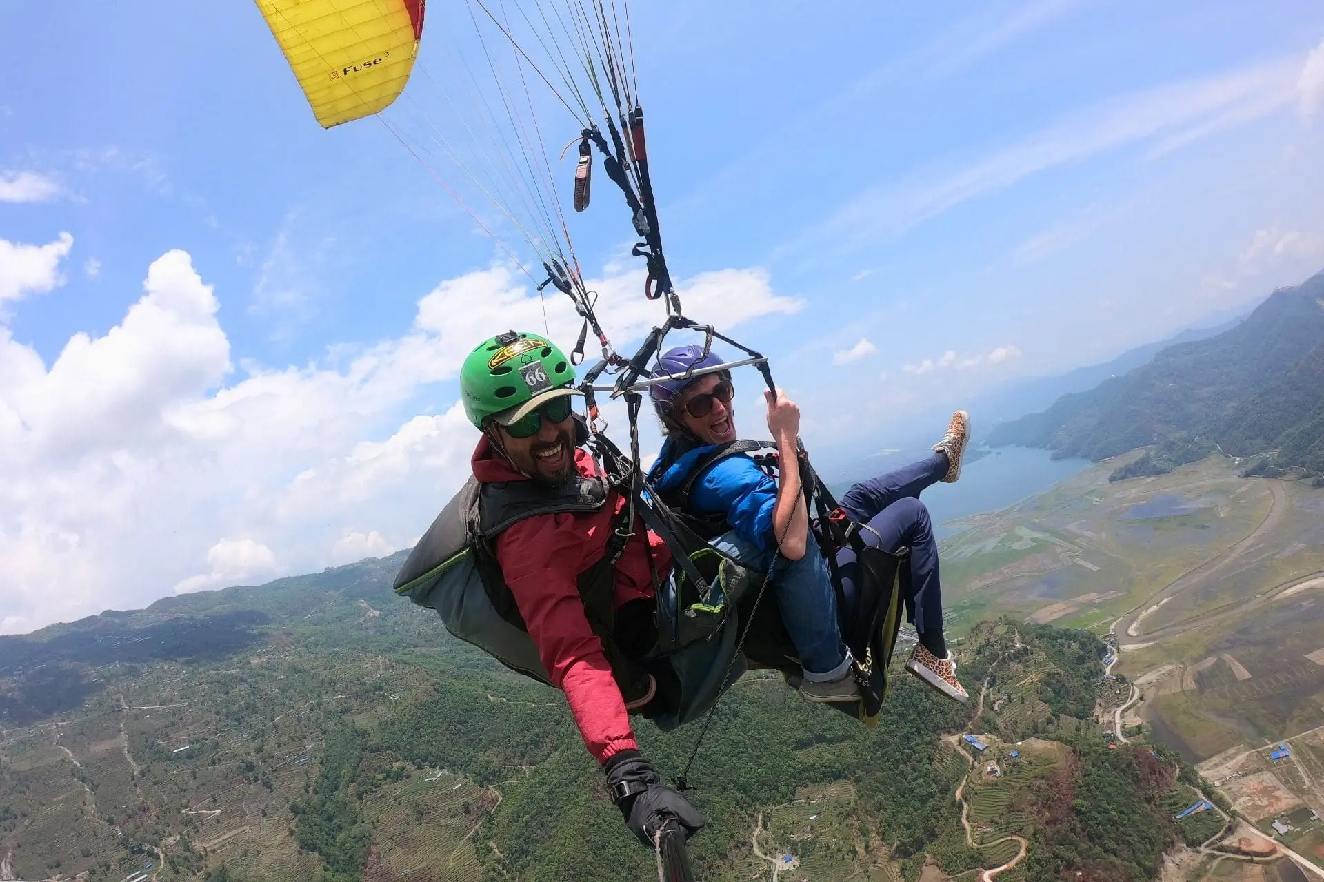 Tandem paragliding high above Pokhara Valley in Nepal with aerial views of farmland, rivers and surrounding hills.