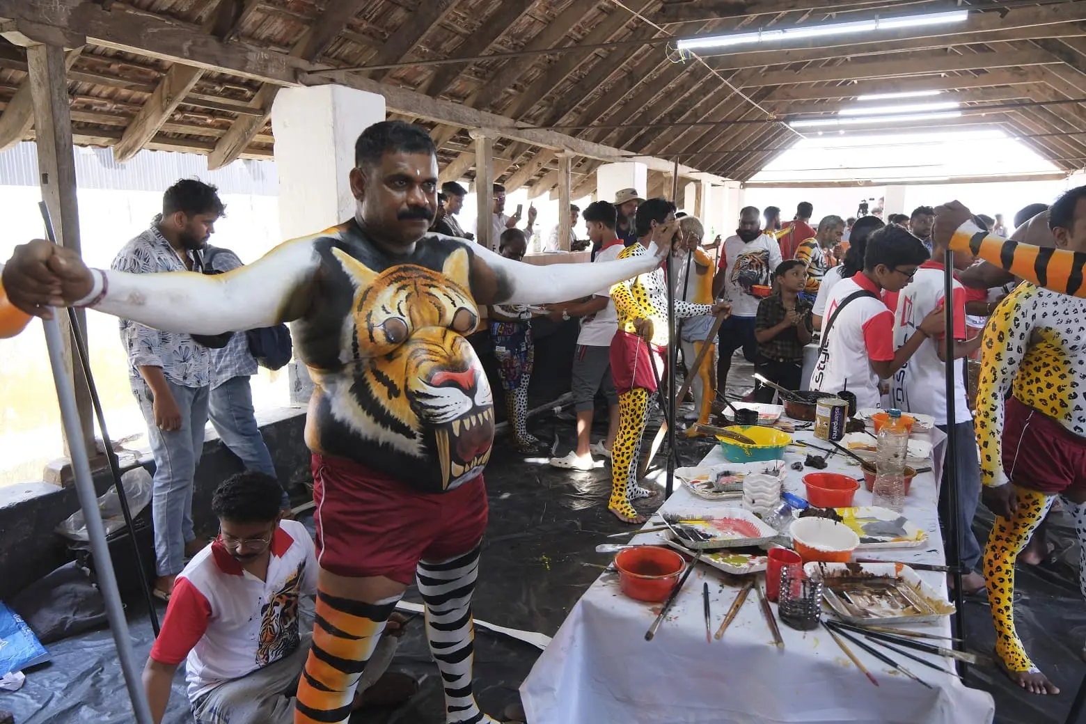 Pulikali performers preparing with body paint in communal hall in Kerala India
