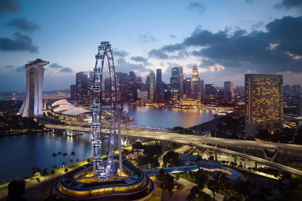 Singapore skyline at Marina Bay including Ritz Carlton hotel with illuminated skyline and Singapore Flyer at dusk