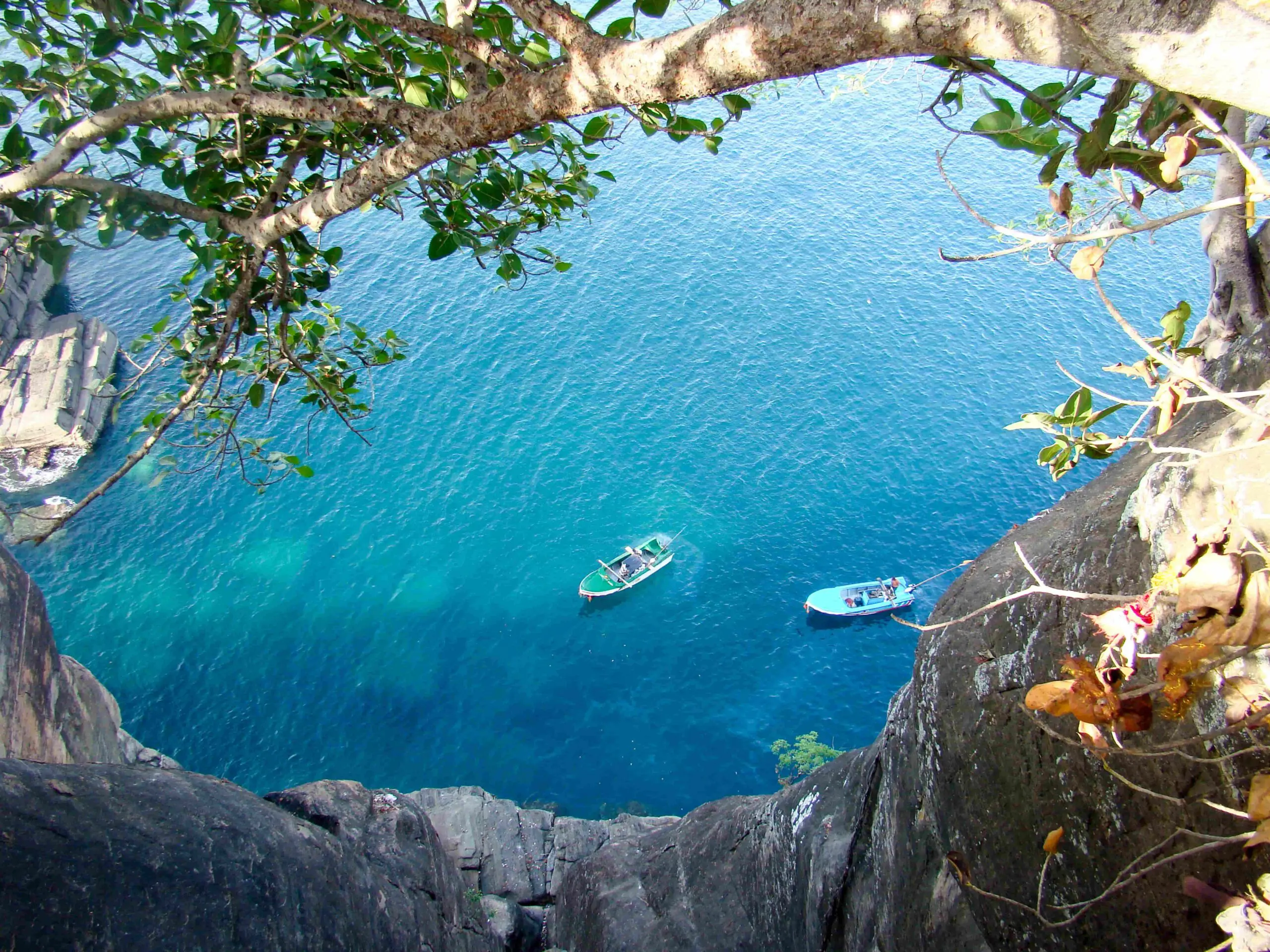 View from rocky cliff over turquoise sea with small boats below