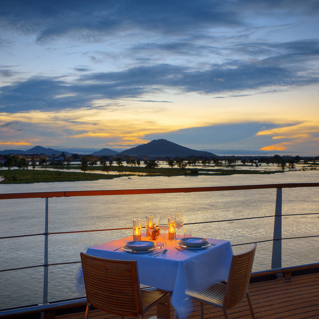 Romantic outdoor dining setup on Aqua Mekong cruise deck at sunset overlooking the Mekong River
