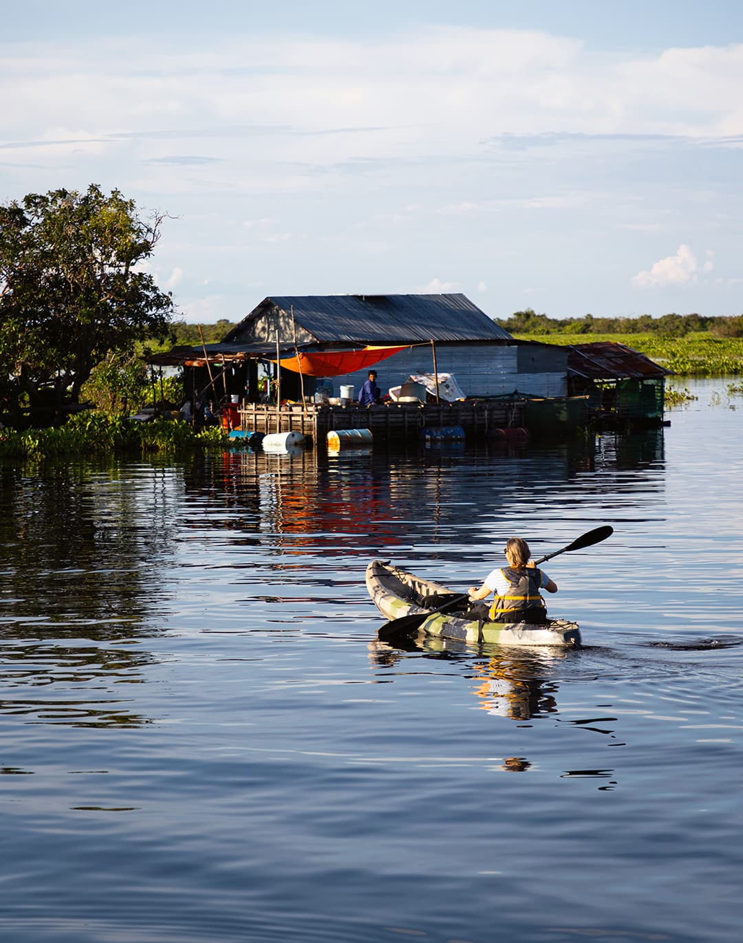 Guest kayaking past floating homes on the Mekong River during an Aqua Mekong excursion