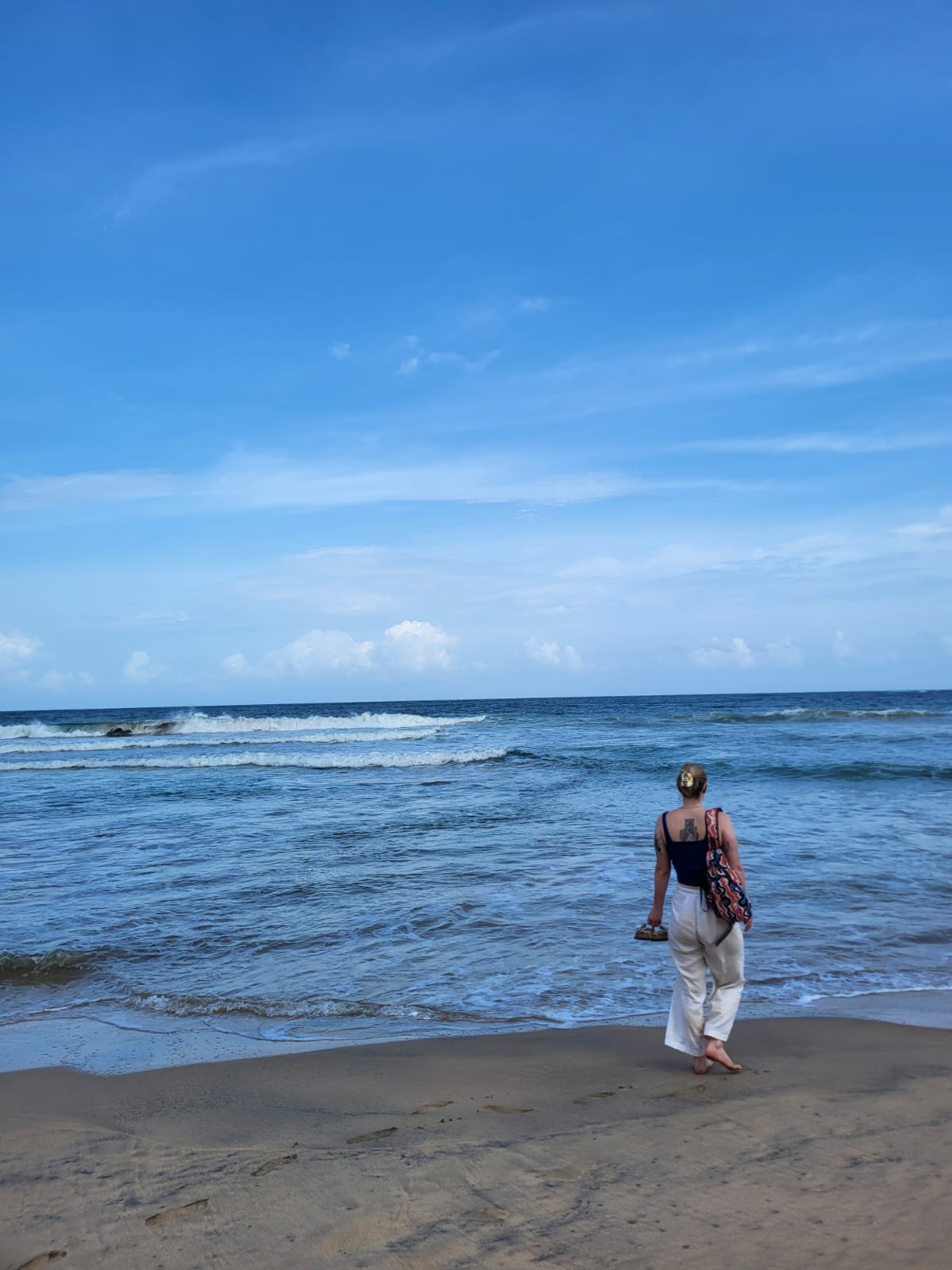 A person standing at the shoreline on a Sri Lankan beach with blue sea and sky, waves breaking behind them